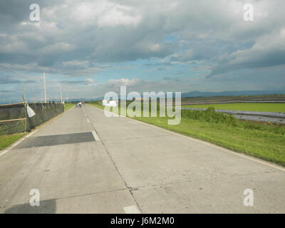 Das Bild bezieht sich auf die Reisfelder in Candaba, Pampanga, Philippinen, bei Salapungan und Magumbali. Diese Felder sind von entscheidender Bedeutung für die lokale Landwirtschaft, in der Reis in abschüssigem Gelände angebaut wird. Die Straßen, die diese Gebiete verbinden, sind für den Güter- und Personentransport in dieser landwirtschaftlichen Region von entscheidender Bedeutung. Stockfoto