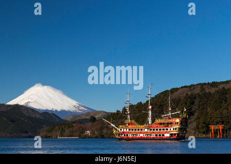 Die hoch aufragenden schneebedeckten Mt. Fuji, das Piratenschiff und einem Tor des Hakone-Schreins gesehen vom Moto-Hakone Hafen am See Ashi. Stockfoto