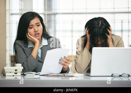 zwei Geschäftsfrauen schauen hoffnungslos ihr Dokument mit der Hand auf den Kopf im Büro Stockfoto