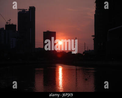 Ein malerischer Blick auf den Sonnenuntergang über Makati und Mandaluyong City in Metro Manila, der die goldenen Farbtöne beim Sonnenuntergang hinter der Skyline einfängt. Das Bild spiegelt die städtische Schönheit und Lebendigkeit der Zwillingsstädte auf den Philippinen wider. Stockfoto