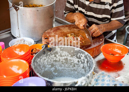 GEORGE TOWN, MALAYSIA - 23. März 2016: Man schneidet Schweinefleisch für Reisbrei auf dem Markt am 23. März 2016 in George Town, Malaysia. Stockfoto