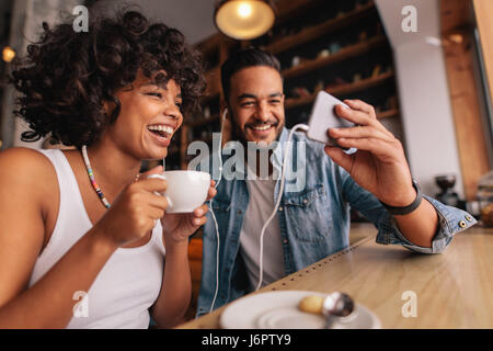Junger Mann zeigen etwas auf Handy zu seiner Freundin im Café. Glückliches junges Paar sitzt im Coffee Shop mit video-Chat auf dem Handy. Stockfoto