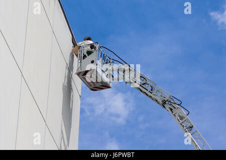 Imker auf einer Hubarbeitsbühne Erfassung ein Bienenschwarm an der Wand. Viele Bienen fliegen herum. Stockfoto