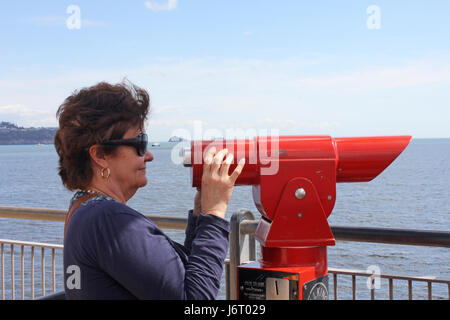 Frau, die durch eine Münze betrieben Teleskop auf einem Steg am Meer im Vereinigten Königreich Stockfoto