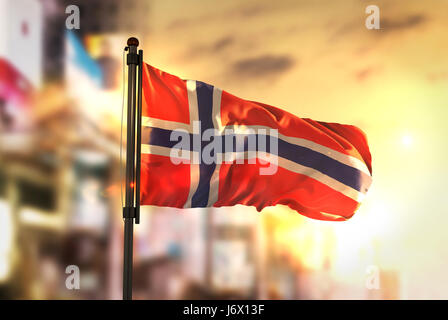 Norwegen Flagge gegen City unscharf Hintergrund bei Sonnenaufgang Hintergrundbeleuchtung Stockfoto