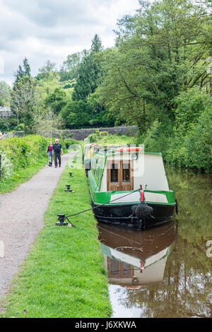 Narrowboats vertäuten auf dem Brecon Monmouth Canal bei Talybont auf Usk. Zwei Personen gehen den Treidelpfad. Stockfoto