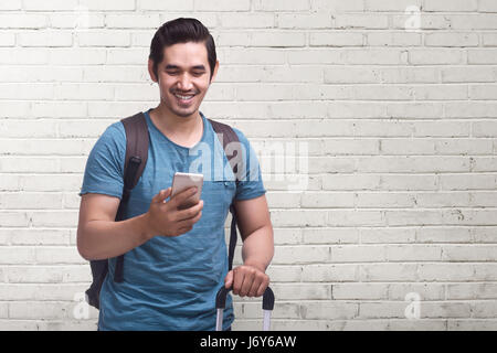 Junge asiatische Reise mit Handy tragen Koffer gegen weiße Wand Hintergrund Stockfoto