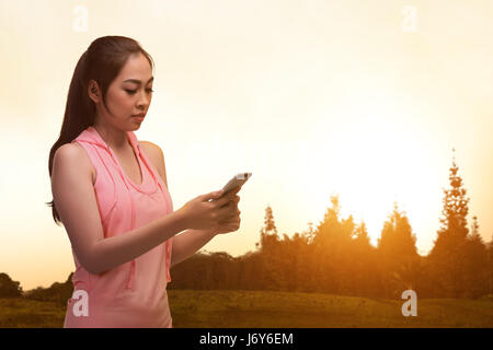 Junge asiatische Sportler Frau mit Smartphone nach dem Training im Freien bei Sonnenuntergang Stockfoto