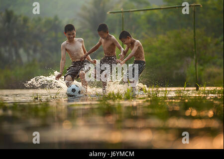 Drei Jungs spielen Fußball in einem aufgeweichten Feld, Thailand Stockfoto