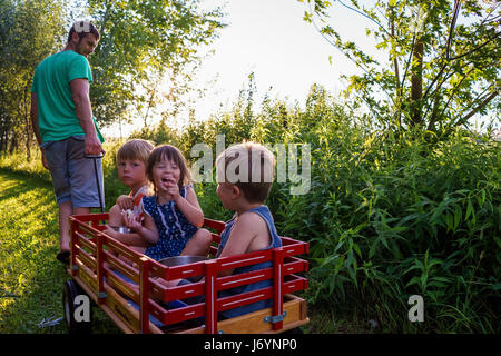 Vater zieht drei Kinder in einem Wagen Stockfoto