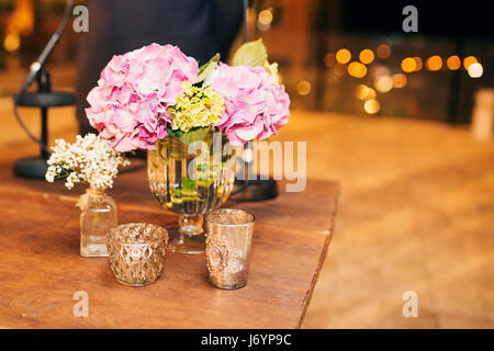 Blumen in Glasvasen mit Kerzen auf Holztisch Stockfoto