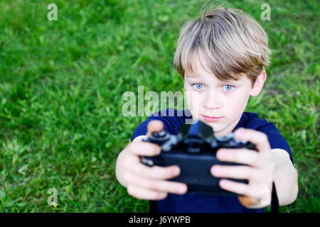 Kind junge Selfie mit einem Retro-Entfernungsmesser Kamera im Freien. Kleines Kind blonde junge mit einer alten Kamera Foto von sich selbst. Kind unter einem p Stockfoto