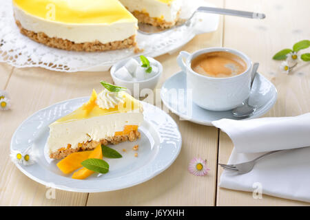 Frischen Käsekuchen mit Mango-Frucht-Glasur, machte der Tortenboden von Cookie-Krümel, serviert mit einer Tasse Kaffee Stockfoto
