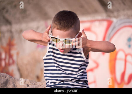 Lustige kleine Junge in einer Sonnenbrille und Streifen Matrosenhemd auf Graffiti wall Hintergrund Stockfoto