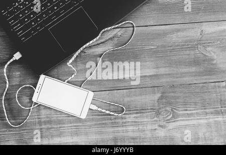 Arbeitsplatz mit Laptop und laden leer Smartphone auf Schreibtisch aus Holz Stockfoto
