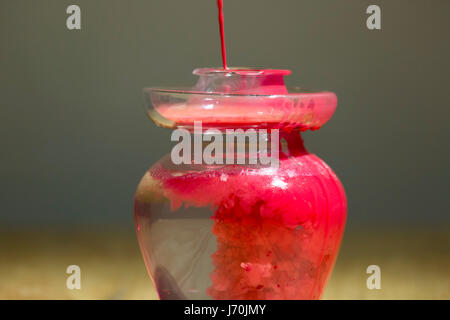 Rote Farbe ins Wasser in einen Glaskrug fallen. Stockfoto