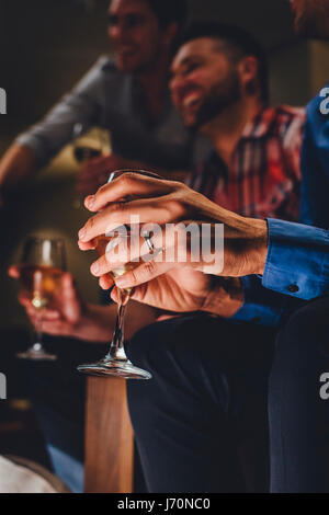 Nahaufnahme von einem mans Händen mit einem Glas Wein in einer Bar. Es gibt zwei Männer Lachen im Hintergrund. Stockfoto