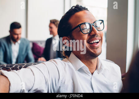 Aufnahme eines Geschäftsmannes in einem Gespräch mit jemanden lachen hautnah. Zwei Männer in Anzügen können reden im Hintergrund gesehen werden. Stockfoto