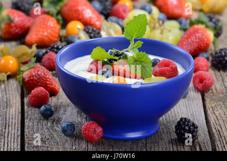 Joghurt mit gemischten frischen Früchten in einem blauen Keramikschale auf einem Holztisch Stockfoto