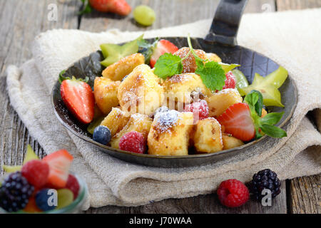 Köstliche österreichische "Kaiserschmarren" (wie zerkleinerte süße Pfannkuchen) serviert mit frischen bunten Früchten in einer eisernen Pfanne auf Vintage Leinen Stockfoto