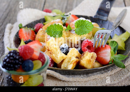 Köstliche österreichische "Kaiserschmarren" (wie zerkleinerte süße Pfannkuchen) serviert mit frischen bunten Früchten in einer eisernen Pfanne auf Vintage Leinen Stockfoto