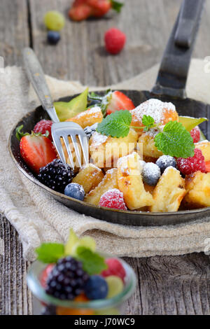 Köstliche österreichische "Kaiserschmarren" (wie zerkleinerte süße Pfannkuchen) serviert mit frischen bunten Früchten in einer eisernen Pfanne auf Vintage Leinen Stockfoto