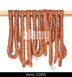 Zeile der geräucherte Schweinswurst im Naturdarm hängen eine Holzstange, isoliert auf weiss trocken Stockfoto