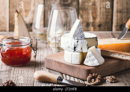 Käseplatte mit Weißwein, Marmelade und Walnüsse auf Holzbrett auf rustikalen Tisch serviert Stockfoto