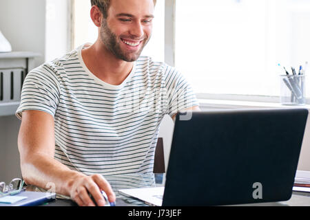 Glücklich junger männlicher Student lächelnd, während hinter seinem Laptop sitzt Stockfoto