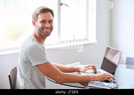 hübschen jungen männlichen Studenten lächelnd in die Kamera hinter Laptop sitzen Stockfoto