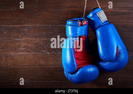Ein paar helle blaue und rote Boxhandschuhe hängt hölzernen Hintergrund. Stockfoto