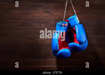 Ein paar helle blaue und rote Boxhandschuhe hängt hölzernen Hintergrund. Stockfoto