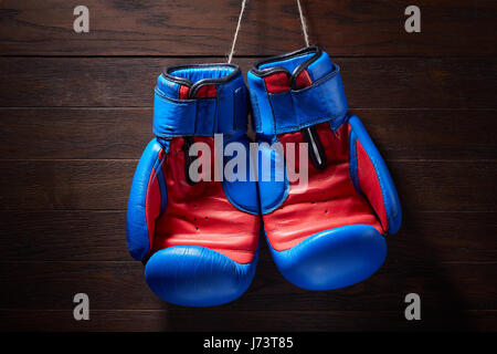 Boxhandschuhe Blau und rot auf einem hölzernen Hintergrund von Seilen hängen. Stockfoto