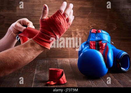 Sportlicher Mann seine Hände mit Bandagen und Boxhandschuhe auf Holzbrett einwickeln. Stockfoto