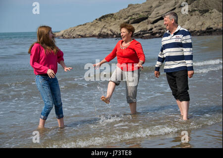 Eine Familie von Mutter, Vater und Tochter im Teenageralter mit ihrem Hund, Paddeln im Meer an einem Strand in Devon. Stockfoto