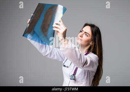 Ärztin untersucht ein Röntgenbild. Schwerpunkt liegt auf dem Röntgenbild. Isoliert auf grauem Hintergrund. Stockfoto