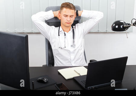 Foto von einem müden jungen männlichen Arzt in seinem medizinischen Büro Stockfoto