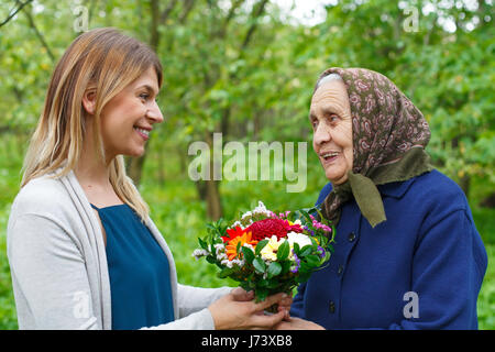 Glückliche alte Frau Blumen von ihrer Enkelin Stockfoto