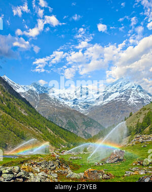 Regenbogen im Bewässerungswasser Tüllen im Sommer Alpen Berg (Schweiz, in der Nähe von Zermatt). Malerische Landschaft mit friedlichen Morgen blau bewölktem Himmel. Stockfoto
