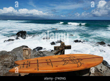 Surfbrett aus Holz und Stein überqueren, ein Denkmal für Surfer Brennan Tristan an der Küste am Hookipa Beach Park, Paia, Maui, Hawaii. Stockfoto