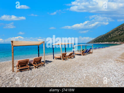 Sommer-morgen-Strand mit türkisblauem Wasser, blauen Wolkenhimmel und Sonnenliegen (Albanien Riviera). Stockfoto