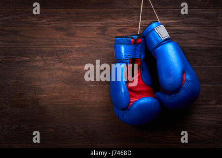 Ein paar helle blaue und rote Boxhandschuhe hängt hölzernen Hintergrund. Stockfoto