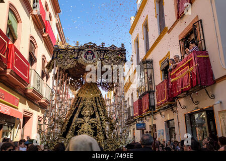 Paso der Jungfrau Maria, durchgeführt durch die Straßen von Sevilla während Menschen Trow Blumen während einer Osterprozession. Stockfoto