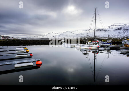 Boote auf einem kleinen Pier in den Osten Fjorden Islands an einem bewölkten Wintertag verankert. Stockfoto