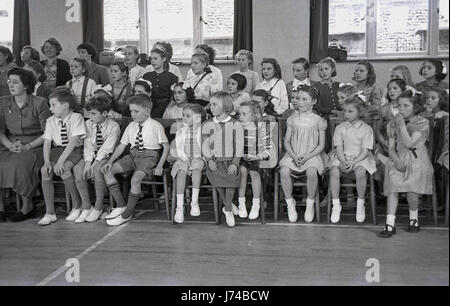 1950, ein Publikum von Kindern der Grundschule, sehen Lehrer und Eltern eine Musik und Bewegung Leistung in der Schule Hall, England, UK. Viele der Kinder tragen auf ihren Füßen weiße Fitness Schuhe ot Pumpen genannt wurden. Stockfoto