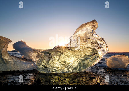 Sonnenaufgang von einem sehr klaren Tag über die Stücke Eis Schuppen aus den Jokullsarlon-Gletscher an der Küste am Jökulsárlón Eis Strand gedrängt. Stockfoto