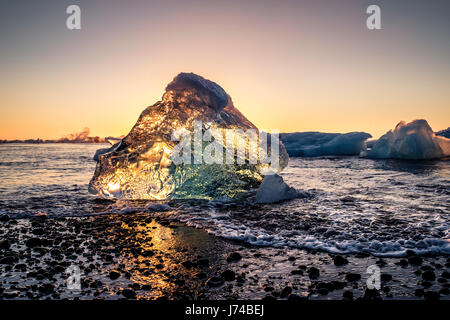 Sonnenaufgang von einem sehr klaren Tag über die Stücke Eis Schuppen aus den Jokullsarlon-Gletscher an der Küste am Jökulsárlón Eis Strand gedrängt. Stockfoto