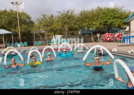 Gruppe des Lächelns glücklicher Frauen in Führungspositionen Teilnahme an Wasser-Aerobic-Kurs, mit Styropor "Wasser Nudeln", beheizten Außenpool. Stockfoto