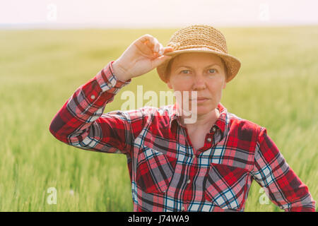 Bäuerin posiert in kultivierten Weizenfeld, Frau Agronom mit Strohhut und kariertes Hemd Inspektion Getreide Ernte Plantage Stockfoto