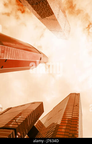 Niedrigen Winkel Blick auf moderne Glas reflektierende Büro Wolkenkratzer gegen bewölkten Himmel und Sonne Licht. Hell Sepia getönten Bild Stockfoto